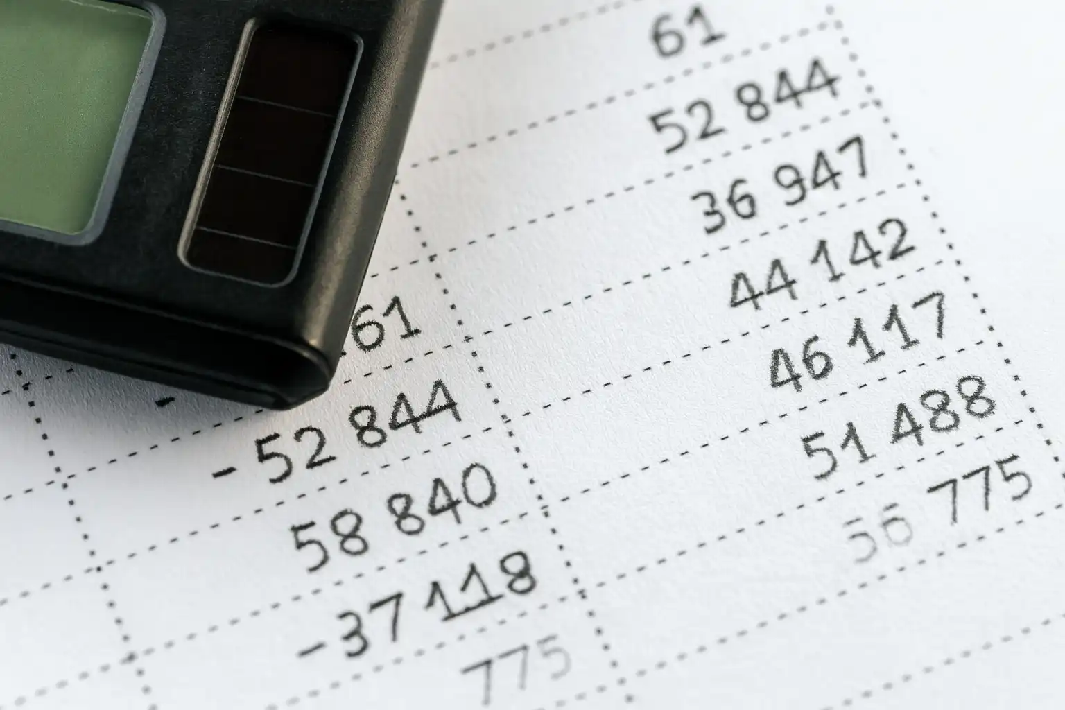 近距离拍摄的财务数据表格与计算器，突出银行流水翻译中的金额核对、数字一致性和版式对照等关键要素。